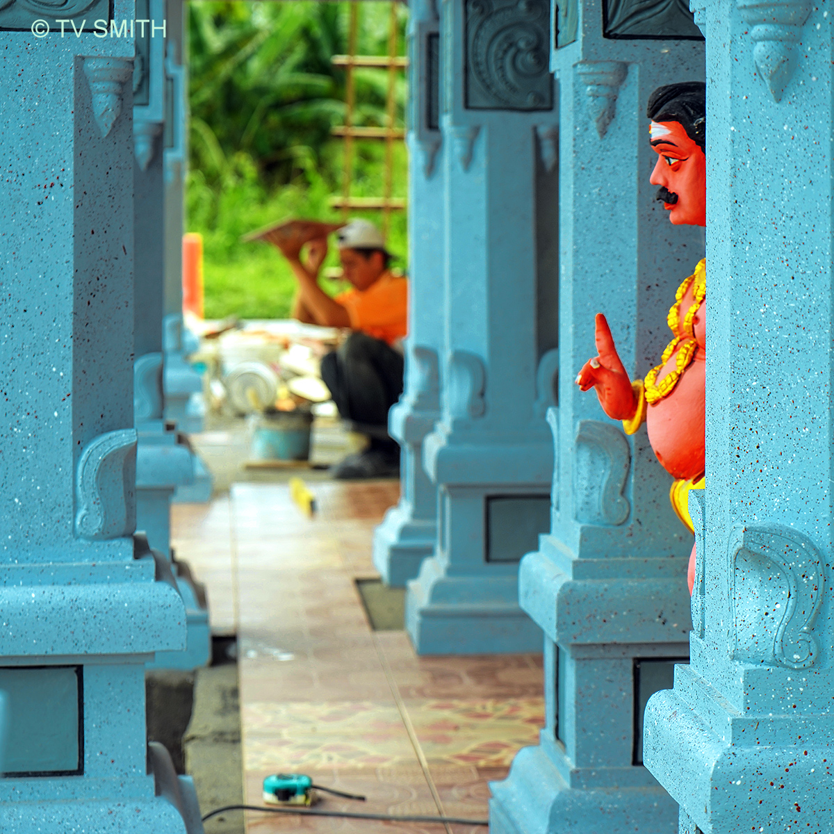 Hindu Temple Statue Supervising A Chinese Tile Installer
